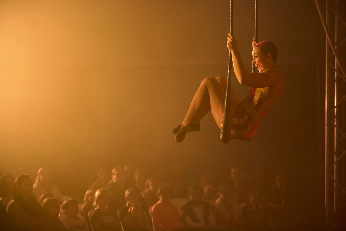 Woman on trapeze in front of crowd with yellow lighting