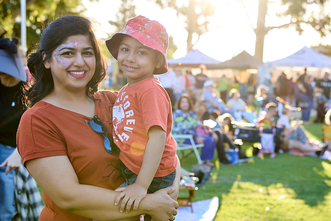 A women smiling and holding her son at a community event.