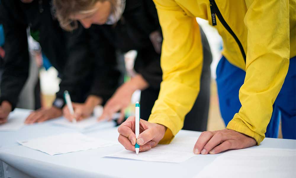 Person in yellow jacket completing a petition at a white table