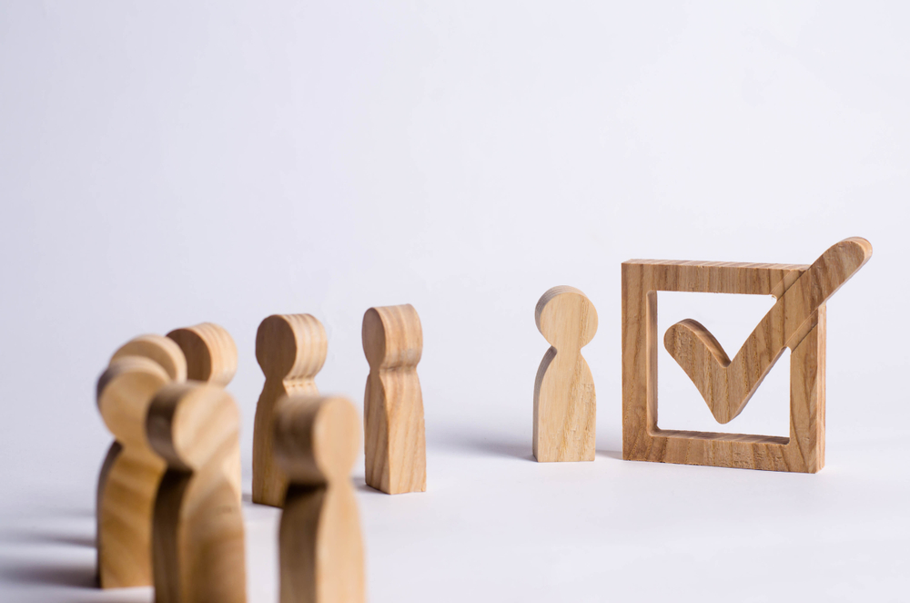 Wooden figures surrounding a ticked box.