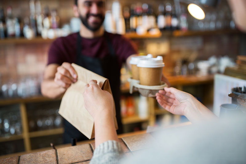 Woman receiving paper bag and coffee from barista 