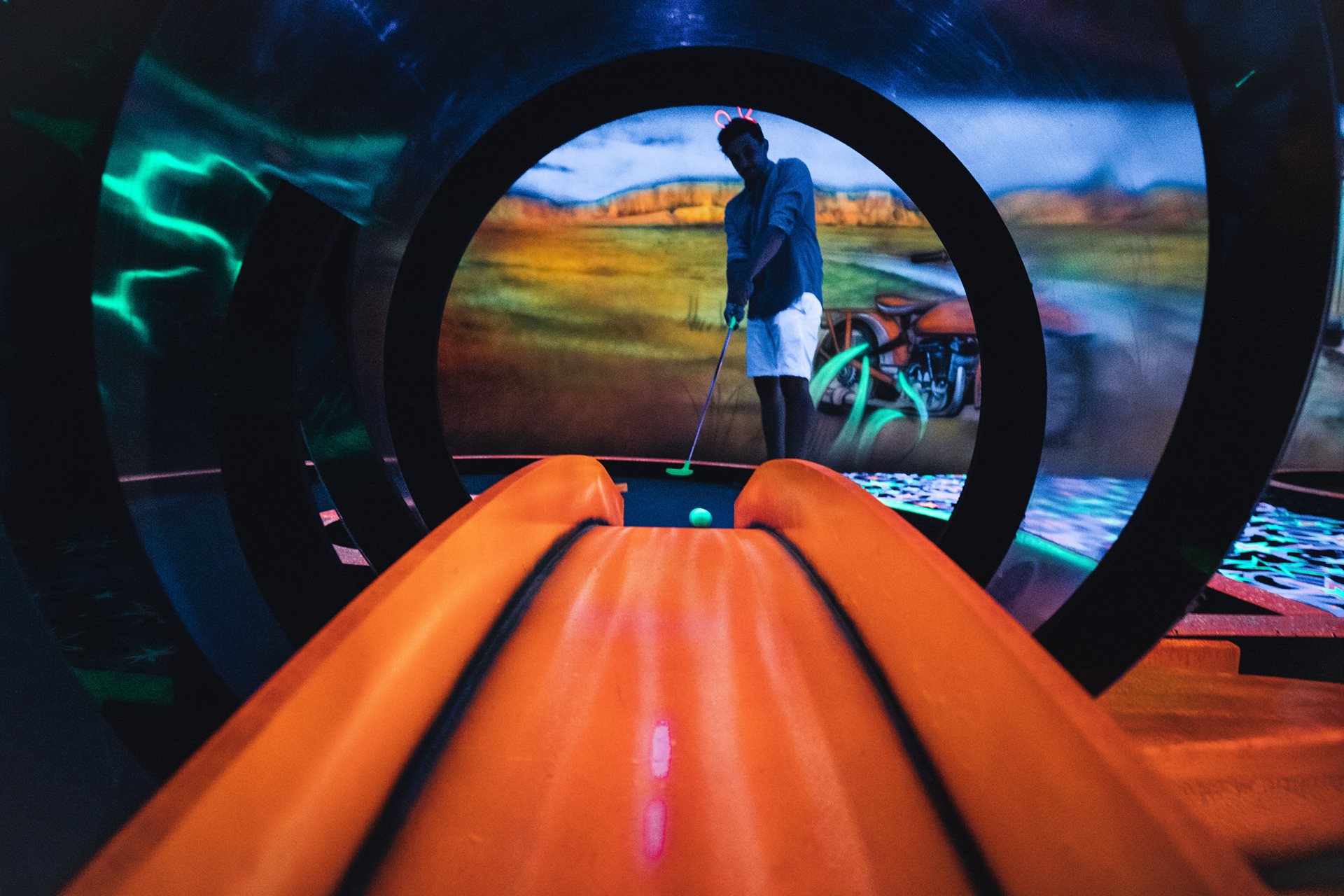 A man playing minigolf under neon lights