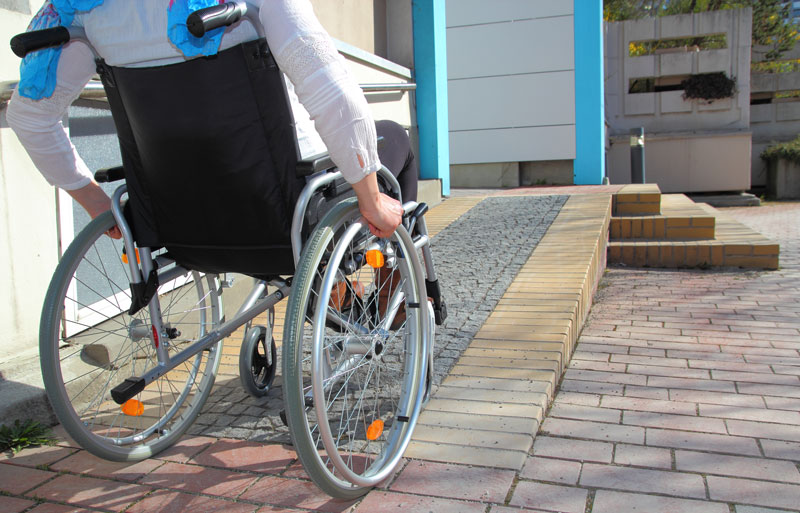 Man in wheelchair going up a paved ramp