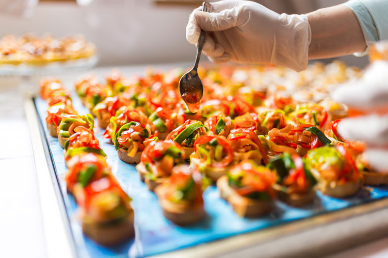 Gloved hand applies sauce to canapes during preparation 