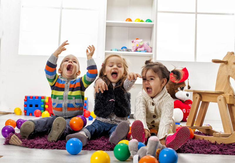Three young children playing with coloured balls inside