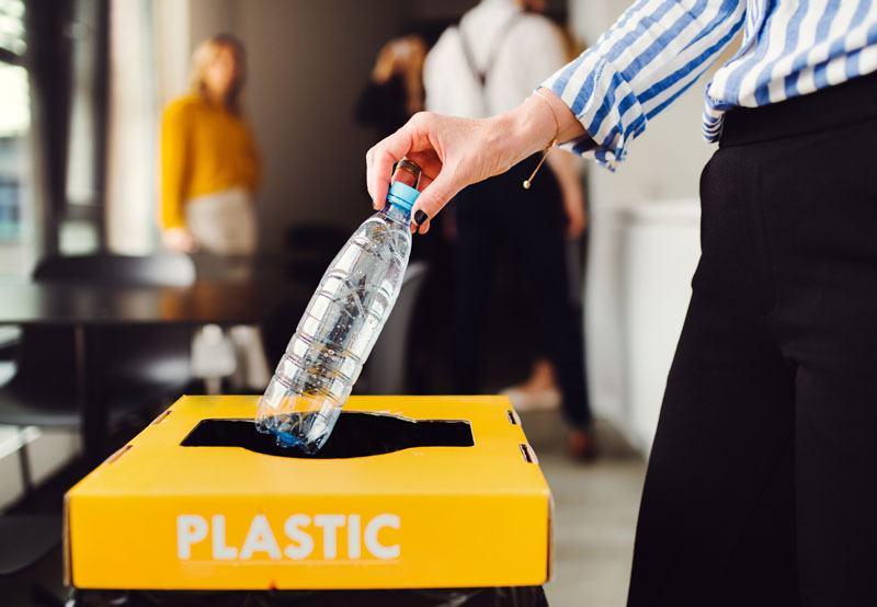 Woman in office putting plastic bottle into recycling 