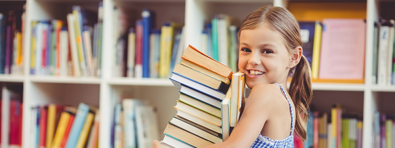 Young girl smiling while holding a stack of books.