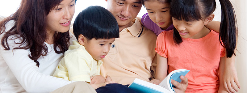 Asian family reading a book together.