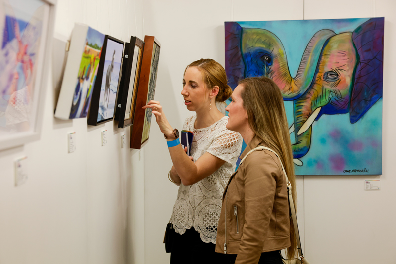 Two women looking at artworks on the wall. One of them is pointing at a detail in one of the artworks.