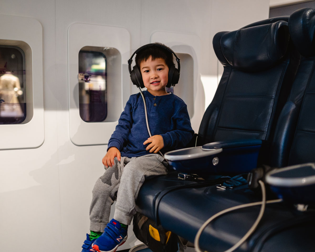 Young boy sitting at aeroplane exhibit.