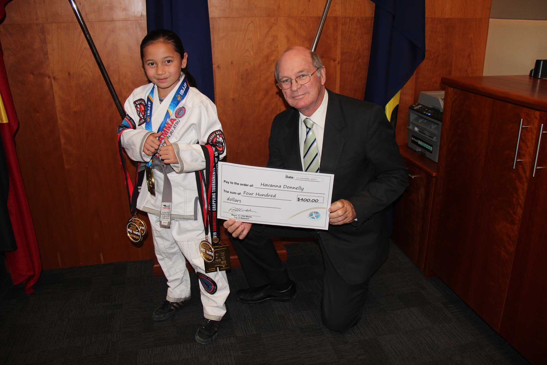 Mayor Councillor Phil Marks presents a sporting donation to a girl holding medals.