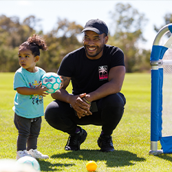 Child with a ball standing next to smiling parent