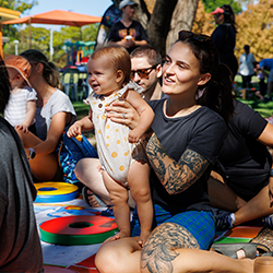 Parent holding a smiling baby at an outdoors wiggles n giggles session