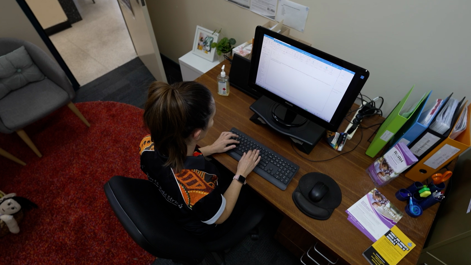 RUAH worker sittin at desk on computer with binders and other documents.