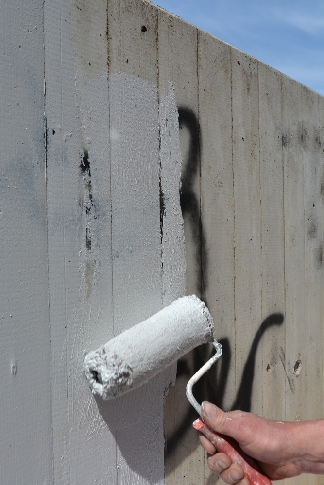Graffiti on a fence being painted over.